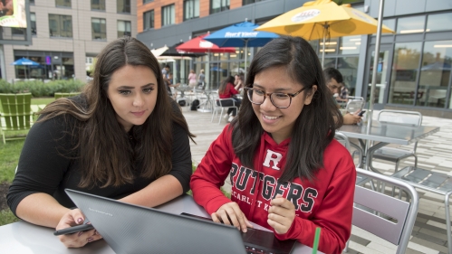 Two students look at a laptop while sitting at a table in The Yard