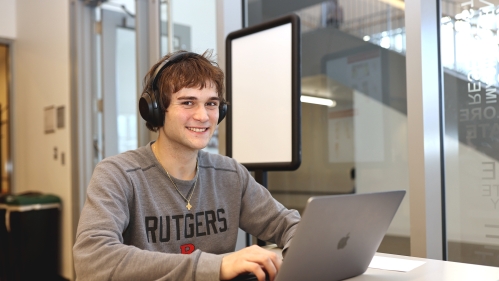 A student wearing headphones and a gray Rutgers shirt types on a laptop in the learning centers.