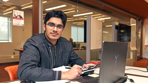 A student with short black hair and wearing a black jacket studies at a laptop in the Learning Centers