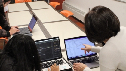 An academic coach points to a computer screen while a student looks on