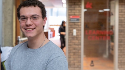 A student with curly short hair and a gray tshirt stand outside the Learning Center