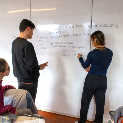 Two students write on a white board while a third student looks on