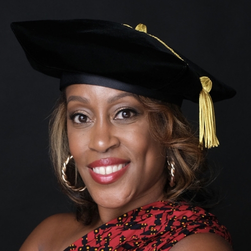 Tasha Coleman has short brown hair and is wearing a doctorate graduation cap with a gold tassle and a red and black dress