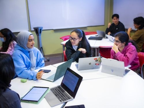 A group of students study with laptops around a table in the learning centers