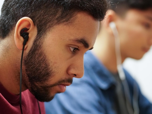 Two students wearing earbuds focus on their laptops while studying