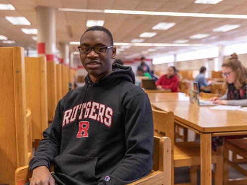 A student wearing a black Rutgers hoodie sits at a study desk