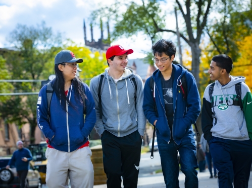 Four diverse students walk along College Avenue in the early fall. 