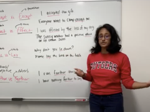 A writing coach in a red sweater stands in front of a white board while teaching