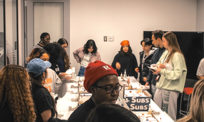 Students get pizza and gather around a table at a night against procrastination event.